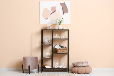 Oturma odasının içinde sedir, ahşap küp takvimi, ev dekorasyonu ve bej duvarın yanındaki raflarda duran vazoda çiçekleri.