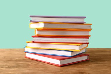 Turkuaz arka plana karşı ahşap masadaki renkli kitap yığını