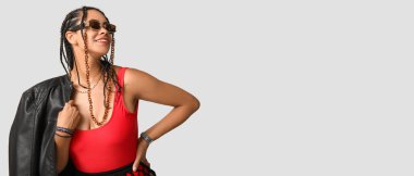 Gri arka planda rastaları olan şık, Afro-Amerikalı bir kadın.