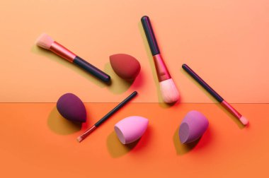 Turuncu arka planda makyaj süngerleri ve fırçalar