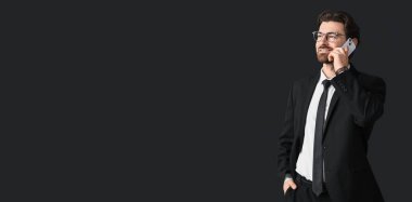 Şık takım elbiseli yakışıklı adam siyah arkaplanda telefonla konuşuyor ve mesaj için yeri var.