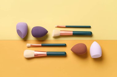 Sarı arka planda makyaj süngerleri ve fırçalar