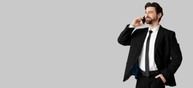 Gri arka planda telefonla konuşan şık takım elbiseli yakışıklı bir adam.