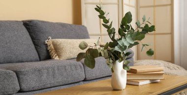 Oturma odasındaki masada okaliptüs dalları olan kitaplar ve vazolar.