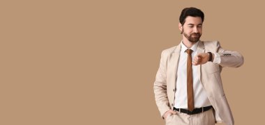 Şık takım elbiseli yakışıklı işadamı bej arkaplanda mesaj için yeri olan saate bakıyor