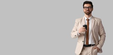 Yakışıklı, şık takım elbiseli, gri arka planda kahve bardağı tutan, mesaj için yeri olan bir adam.