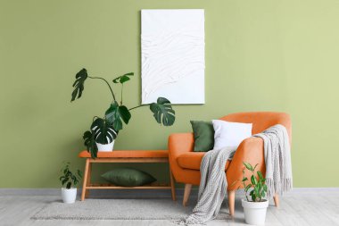 Yeşil duvarın yanında rahat koltuklu, banklı ve çiçekli şık bir oturma odası.