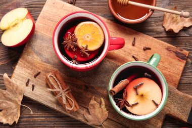 Ahşap arka planda elma ve portakallı sıcak şarap kadehleri.