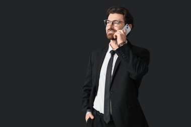 Şık takım elbiseli yakışıklı işadamı siyah arka planda cep telefonuyla konuşuyor.