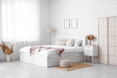 Büyük bir yatağı, masası ve vazolarında otları olan ışık odasının içi.