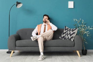 Mavi duvarın yanındaki koltukta cep telefonuyla konuşan yakışıklı bir iş adamı.