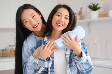 Güzel, genç, mutlu Asyalı kız kardeşler mutfakta sarılıyorlar.