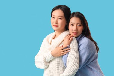 Güzel, mutlu Asyalı kız kardeşler mavi arka planda sarılıyorlar.