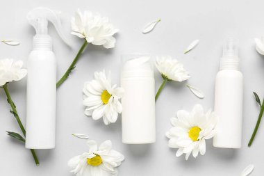 Kozmetik ürünleri ve gri arka planda papatya çiçekleri içeren kompozisyon