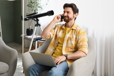 Evdeki koltukta cep telefonuyla konuşan yakışıklı bir adam.