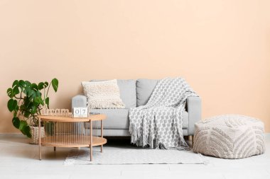 Bej duvarın yanındaki sehpanın üzerinde kanepe, puf ve tahta küpler olan oturma odasının içinde.