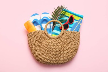 Plaj aksesuarları ve pembe arka planda bir şişe güneş kremi.