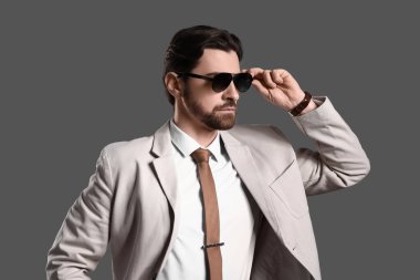Gri arka planda güneş gözlüklü, açık renk takım elbiseli yakışıklı bir genç.
