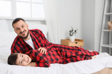 Kareli pijamalı mutlu bir baba oğluyla evde yatakta eğleniyor.