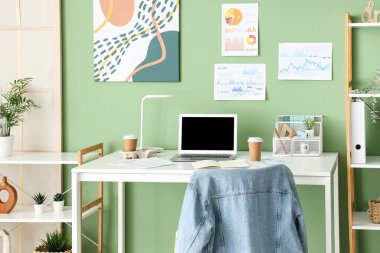 Ofisteki yeşil duvarda boş dizüstü bilgisayarı ve diyagramları olan işyeri