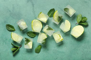 Buz küplerinde donmuş kireç dilimleri ve yeşil arka planda nane yaprakları.