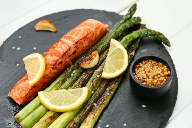 Kızarmış yeşil kuşkonmaz, lezzetli somon ve beyaz ahşap arka planda limon dilimleri, yakın plan.