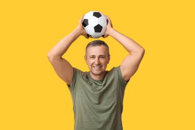 Sarı arka planda futbol topuyla oynayan yakışıklı olgun bir adam.
