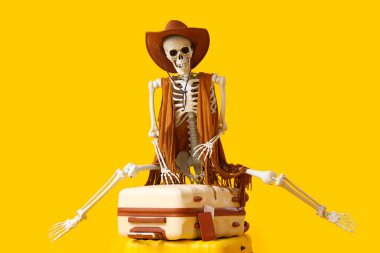 Sarı arka planda bavulları olan kovboy kostümlü insan iskeleti. Seyahat kavramı