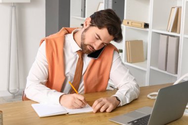 Ofiste cep telefonuyla konuşan defterli yakışıklı bir iş adamı.