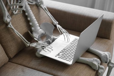 Oturma odasındaki kanepede dizüstü bilgisayarlı iskelet, yakın plan.