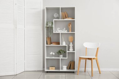 Odada ışık duvarının yanında bitki ve sandalye olan bir kitaplık.