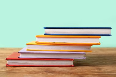 Turkuaz arka plana karşı ahşap masadaki renkli kitap yığını