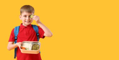 Sarı arka planda sağlıklı yiyeceklerle dolu beslenme çantası tutan şirin bir okul çocuğu.