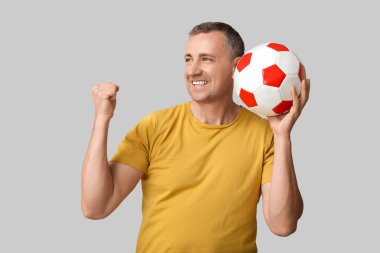 Gri arka planda futbol topu olan mutlu ve olgun bir adam.