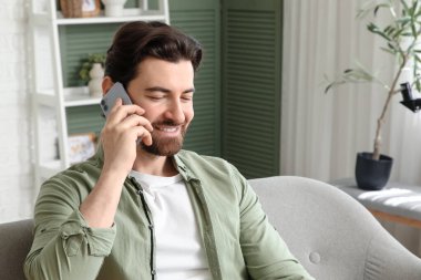 Evdeki koltukta cep telefonuyla konuşan yakışıklı adam, yakın plan.