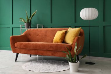 Oturma odasının içindeki yeşil duvarın yanındaki rahat kahverengi kanepe.