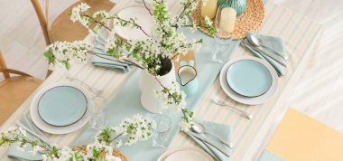 Tabakları, bardakları ve çiçek açan ağaç dalları olan zarif bir masa.