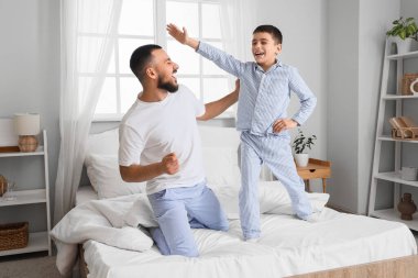 Mutlu baba ve oğlu pijamalarıyla evde yatakta eğleniyorlar.