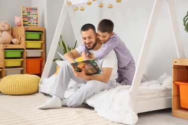 Mutlu baba ve oğlu pijamalarıyla evde kitap okuyorlar.