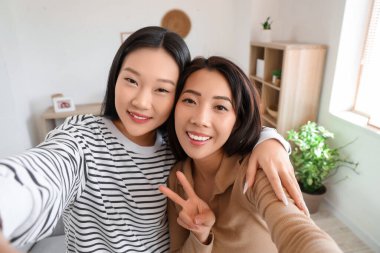 Güzel mutlu Asyalı kız kardeşler evde selfie çekiyorlar.