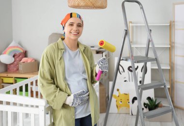 Çocuk odasında tamir sırasında boya silindirli hamile bir kadın.