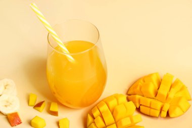 Bir bardak taze mango suyu ve turuncu arka planda dilimlenmiş muz.