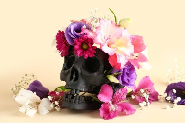 Bej arka planda güzel çiçekleri olan siyah insan kafatası, yakın plan.