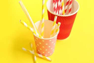 Sarı arka planda farklı pipetli kağıt bardaklar.