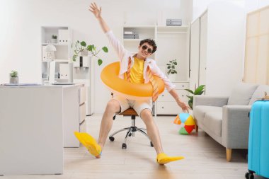 Yüzme yüzüklü ve yüzgeçli genç işadamı yaz tatilini ofiste bekliyor.