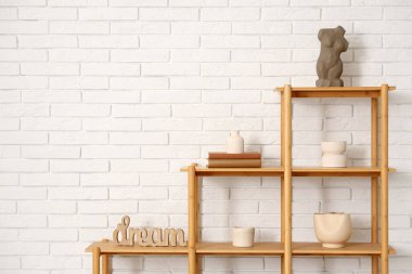 Beyaz tuğla duvarın yanında kitap ve dekor bulunan ahşap raf ünitesi.