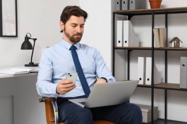 Ofiste cep telefonu ve dizüstü bilgisayarla çalışan yakışıklı bir iş adamı.