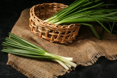 Siyah arka planda taze yeşil soğanlı hasır sepet.