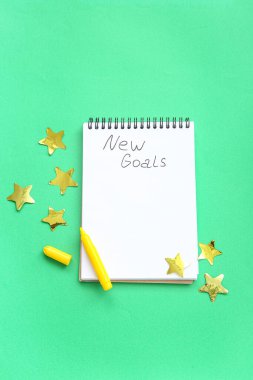 Yapılacaklar listesi boş olan defter, yeşil arka planda işaretleyici ve konfeti. Yeni yıl hedefleri