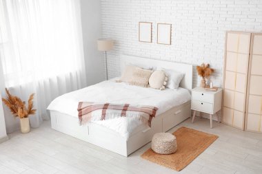 Büyük bir yatağı, masası ve vazolarında otları olan ışık odasının içi.